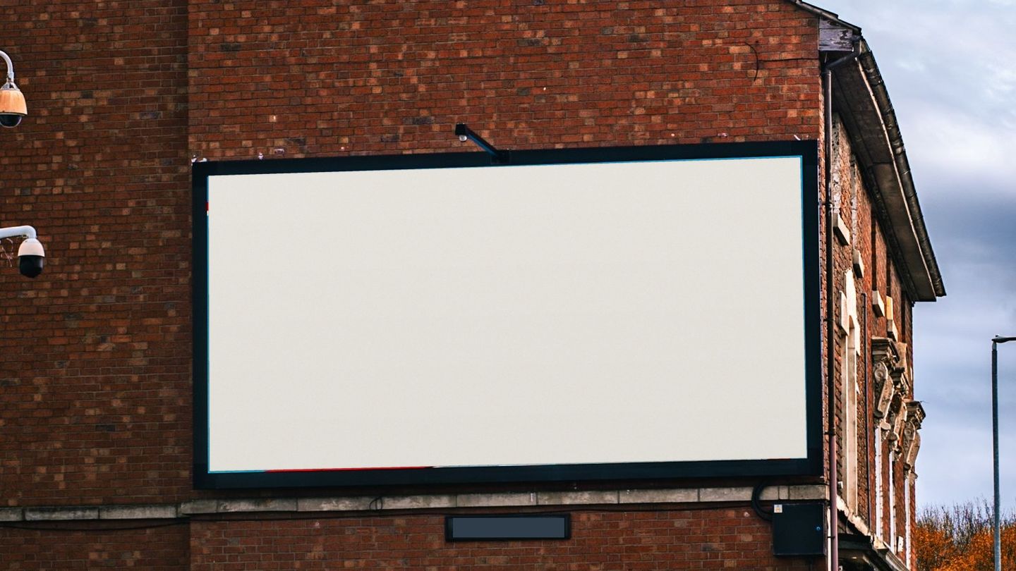 An empty roadside billboard on the gable end of a red-brick building